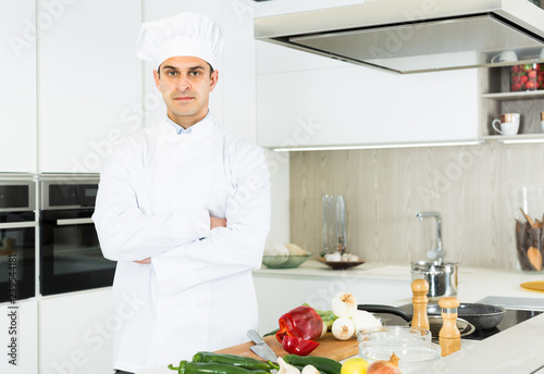 Male chef in white uniform standing near workplace on kitchen