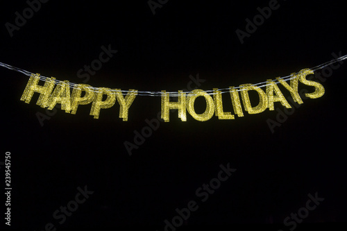 Golden Happy Holidays message in glitter letters with multiple exposure motion blur against empty black night background photo