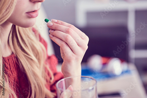 Cute young blonde taking a pill with a glass of water at home
