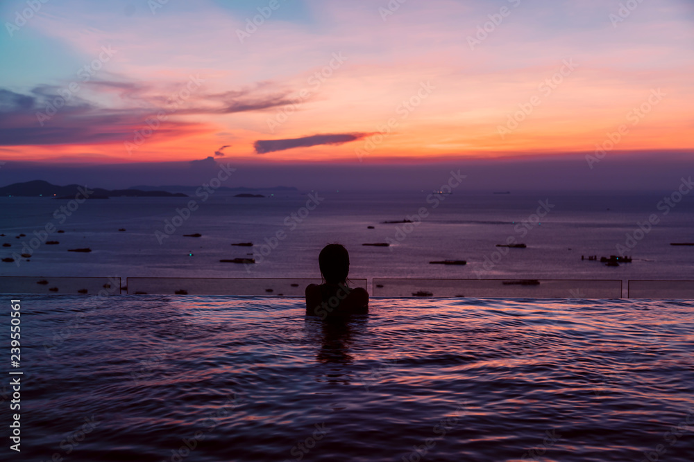 Black silhouette of asian woman on summer vacation holiday relaxing in infinity swimming pool with blue sea sunset view. Healthy happiness lifestyle