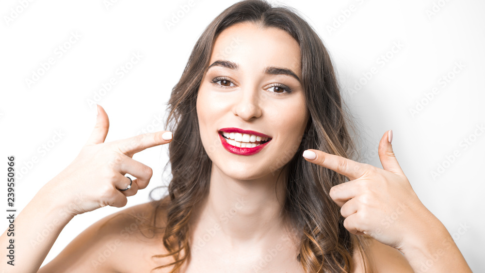 A smiling young woman points to healthy, white, even teeth. Dental concept. A smiling young woman points to healthy, white, even teeth. Dental concept.