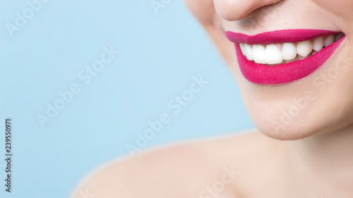 Close-up of a smiling woman with healthy white teeth, red matte lipstick, on a blue background. Dentistry concept. Copy space. 