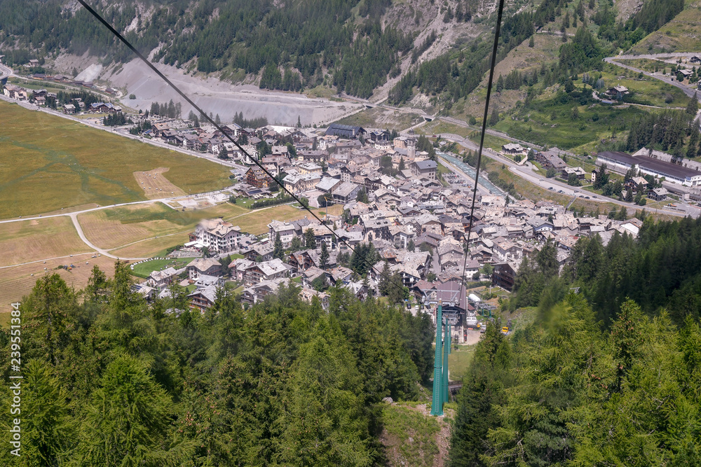 Elevated view from a cable car of a mountain valley in summer with an alpine village and green forest, Cogne, Aosta Valley, Alps, Italy 