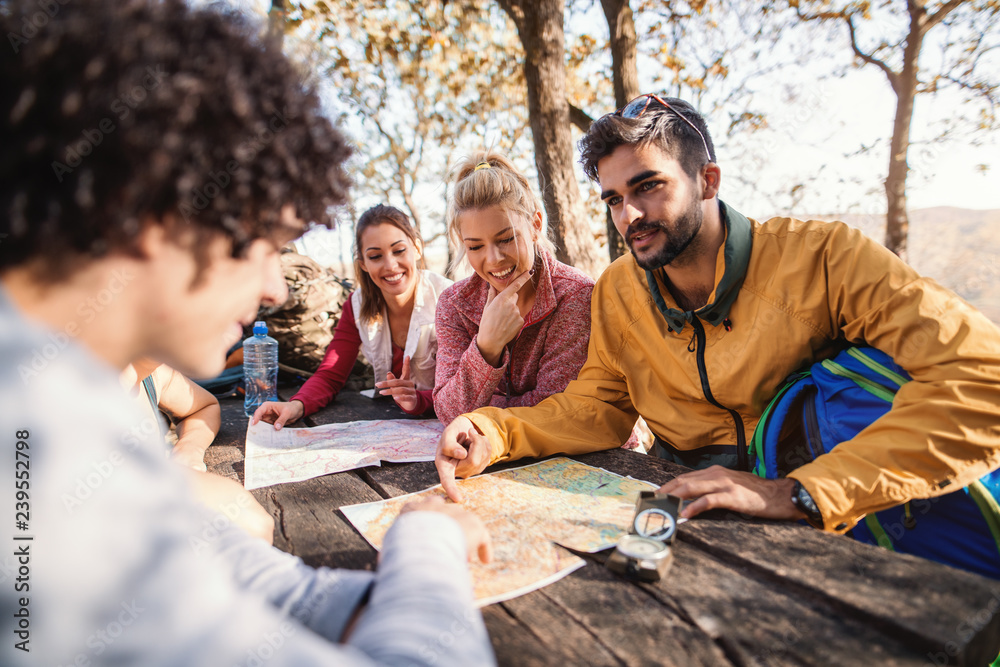 Hikers sitting on the bench at the table in the woods and looking at map. Autumn season.