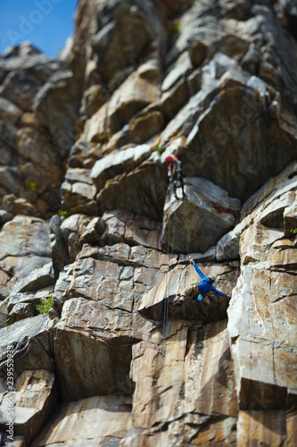 The climber climbs up the rope against the background of a huge rock wall. Two person rope. Tilt-Shift effect. photo