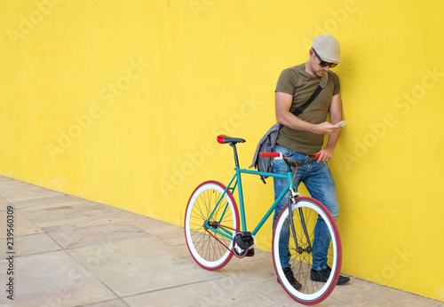 Full length of man using smart phone while standing by bicycle against yellow wall at sidewalk in city
