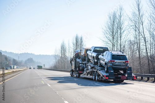 Big rig car hauler semi truck transporting cars on wide divided highway with winter naked trees