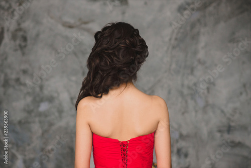 Rear view of elegant woman with bun hairstyle in red evening dress. Portrait on grey background