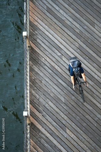 Cyclist in helmet with backpack rides wooden pier along the river