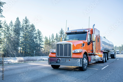Orange big rig semi truck with long tank semi trailer transporting liquid and liquefied chemical cargo on the winter frosty road