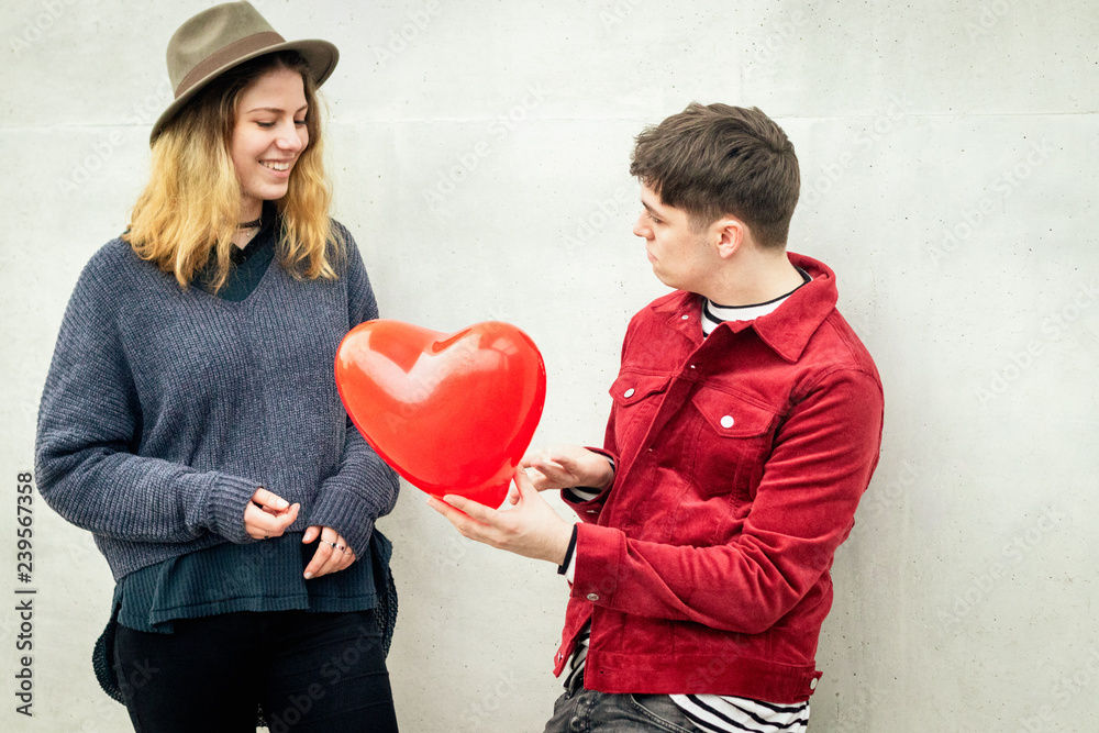 love declaration: young man giving an heart shaped balloon to a blonde girl love declaration: young man giving an heart shaped balloon to a blonde girl