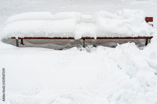 Wooden bench covered with snow in a park waits for companionship.