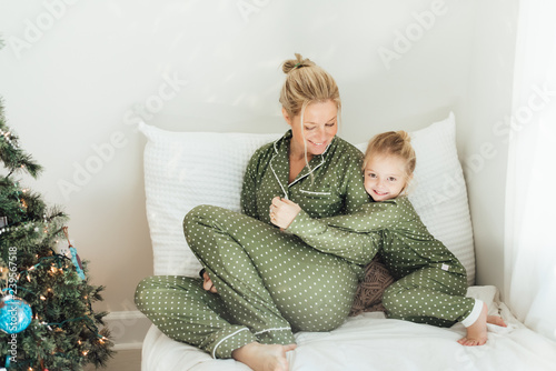 Mother and daughter sitting on a bed next to a Christmas tree