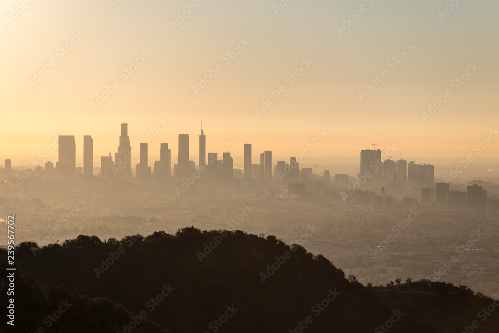 Hazy orange dawn cityscape view of downtown Los Angeles, Hollywood with Runyon Canyon Park hilltop in foreground.    
