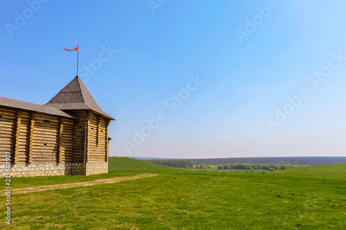 Wooden fortress with tower and flagstaff on a green meadow  at plain