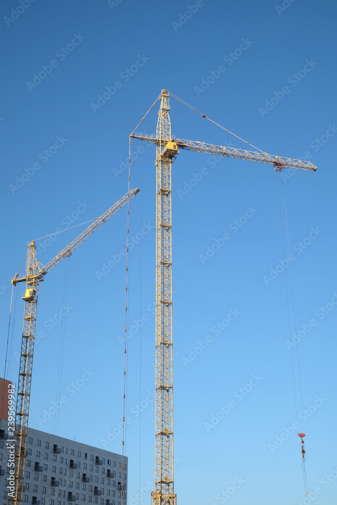 Big yellow construction tower crane on dwelling construction over blue sky