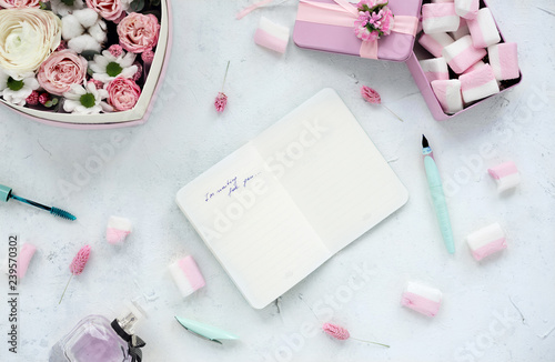 Open notebook on white table with flowers and marshmallow.Pastel colors.Flat lay.Overhead view.