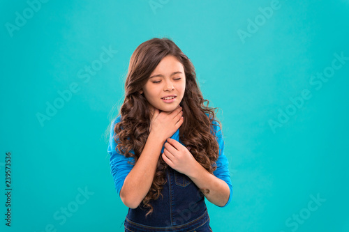 Sore throat remedies. Kid feels pain in throat. Girl cute kid suffer from pain in neck. Girl painful face stand blue background. Health care and medicine. Sore throat remedies. Throat pain treatment