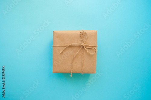 Gift box wrapped in brown colored craft paper and tied with tope on blue background.