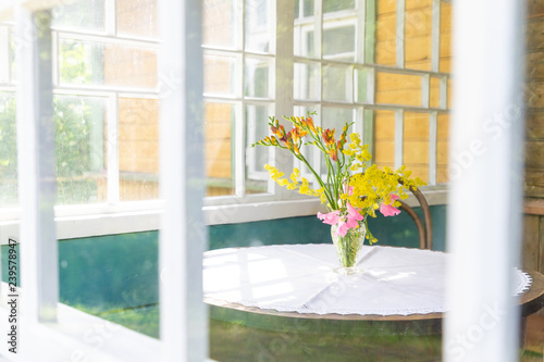 Yellow-pink bouquet of wild flowers on the table. Photo in bright colors. Table and bouquet can be seen through the window of the balcony or veranda.