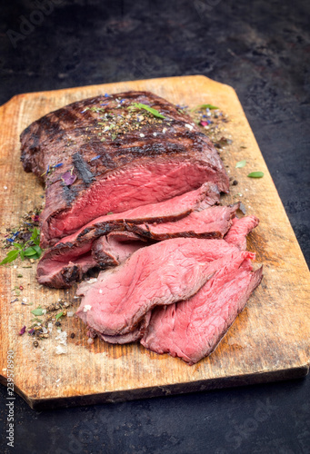 Traditional barbecue dry aged sliced roast beef steak with herbs as closeup on an old cutting board