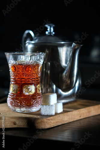 Glass of black tea, on a wooden support, a teapot for tea on a wooden support, white lump sugar on a wooden support. The vertical photo on a black hum noise. Ormud. Turkish ормуд. The Turkish glass fo photo