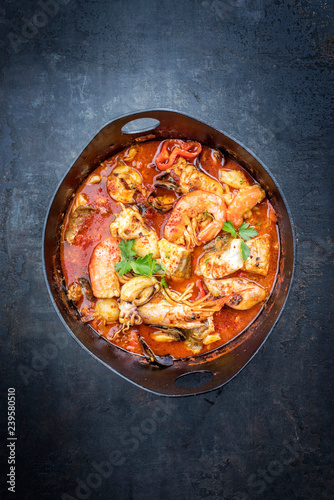 Traditional Spanish sarsuela fish stew with prawns, mussels and fish as top view in a modern design Japanese cast-iron roasting dish
