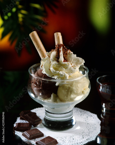 Copa con dos bolas de helado, vainilla i chocolate y nata montada con dos barquillos de adorno.
