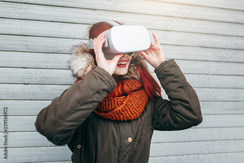 Pretty hipster young girl plays virtual reality mobile game app on smartphone attached to modern VR glasses outdoor in cold winter day