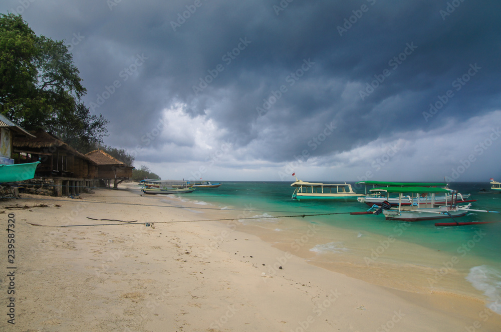 Sandy beach with moored Indonesian boats on the tropical island of Gili Meno. Heavy leaden clouds hung over the beach, a thunderstorm is approaching.