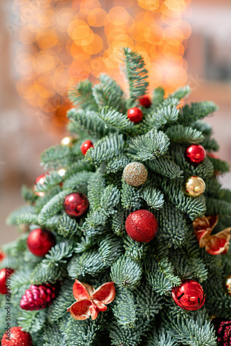 Beautiful small decorated Christmas tree on dark wooden table. Happy mood. Garland bokeh on background. Wallpaper. Danish pine and fir, Nobilis