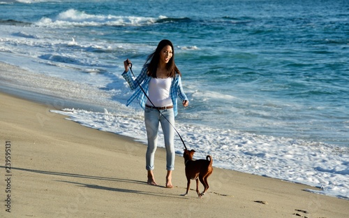 Young barefoot woman is playing with her dog on the beach.