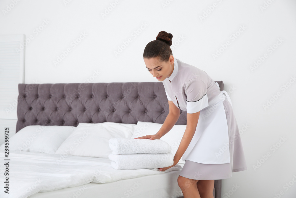 Young chambermaid putting clean towels on bed in hotel room Young chambermaid putting clean towels on bed in hotel room