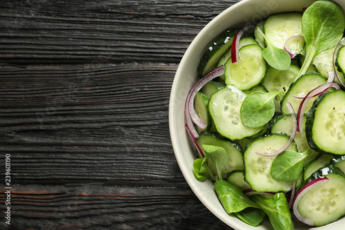 Delicious cucumber salad with onion and spinach in bowl on wooden background, top view. Space for text