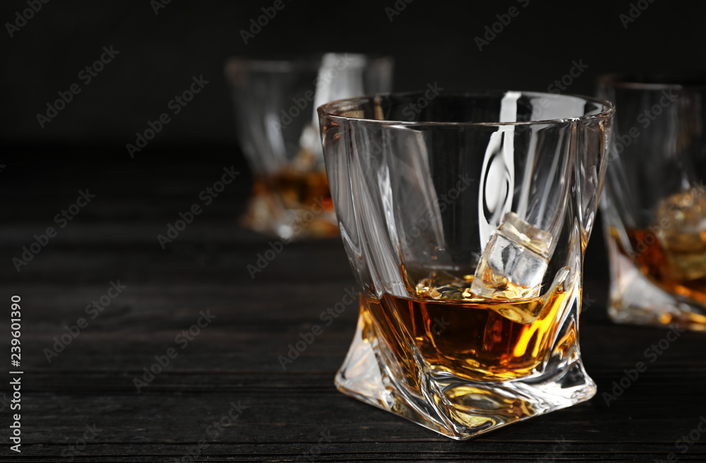 Golden whiskey in glass with ice cubes on wooden table. Space for text Golden whiskey in glass with ice cubes on wooden table. Space for text