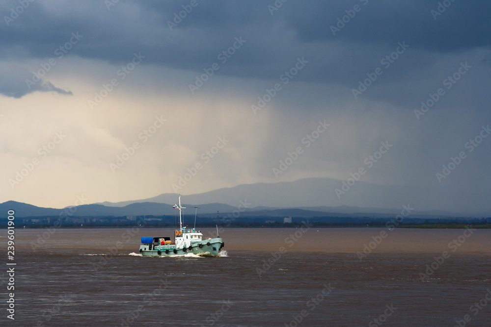 Landscape with a large river, which floats boat. In the sky dark clouds. Gloomy weather, it is raining. Amur River, Khabarovsk Region, Far East of Russia. Landscape with a large river, which floats boat. In the sky dark clouds. Gloomy weather, it is raining. Amur River, Khabarovsk Region, Far East of Russia.