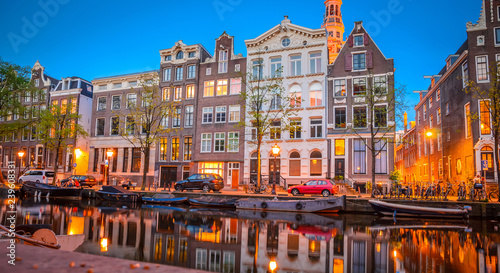 Photography Traditional old buildings and boats at night in Amsterdam, Netherlands