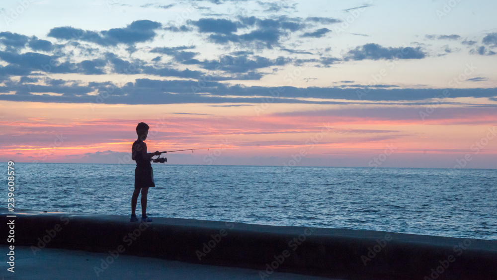 boy fishing from a pier in cuba at sunset