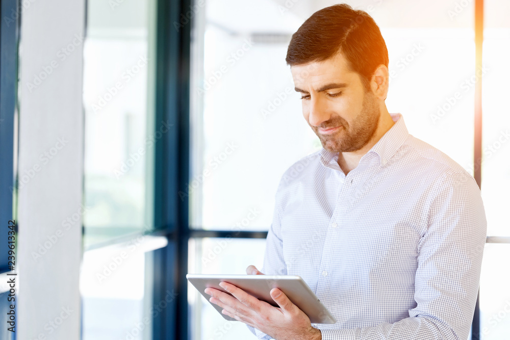 Young handsome businessman using his touchpad standing in office Young handsome businessman using his touchpad standing in office