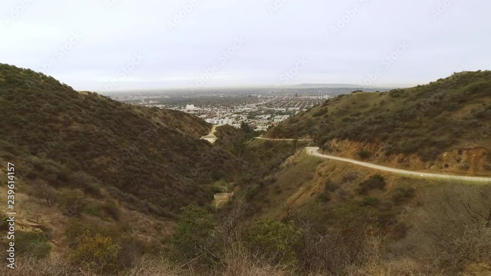 A wide overview establishing shot of Runyon Canyon in the hills of Los Angeles on an overcast day. Hikers on the trail in the distance. A wide overview establishing shot of Runyon Canyon in the hills of Los Angeles on an overcast day. Hikers on the trail in the distance.