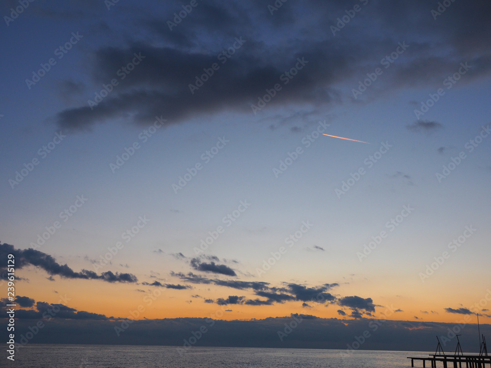 Evening sky after sunset above a sea and little trace of plane among clouds