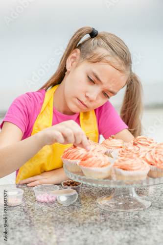 Close up little girl decorates cupcakes at kitchen