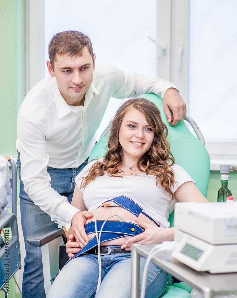 Pregnant woman with her husband checking fetal heartbeat by fetal monitoring Pregnant woman with her husband checking fetal heartbeat by fetal monitoring