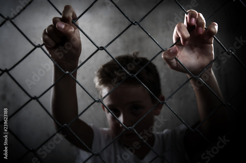 Fotografie Sad serious boy behind a chain link fence