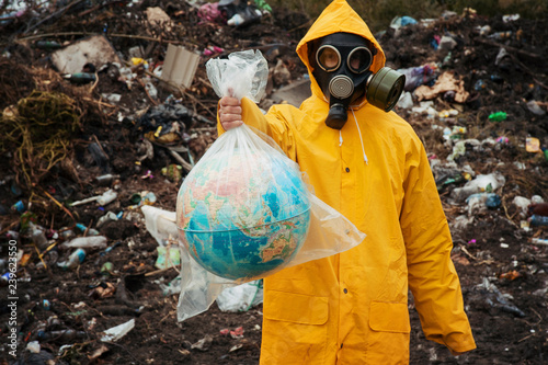 Bilde på lerret Man in  gas mask holds globe in plastic bag at garbage dump