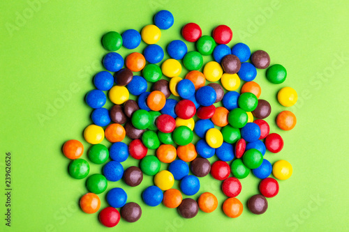 Glazed colored chocolate candies are gathered on bright green background