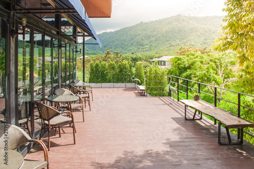 Row of table and chair place on wooden terrace outside of restaurant or coffee cafe with beautiful landscape viewpoint and morning sunlight in the background.