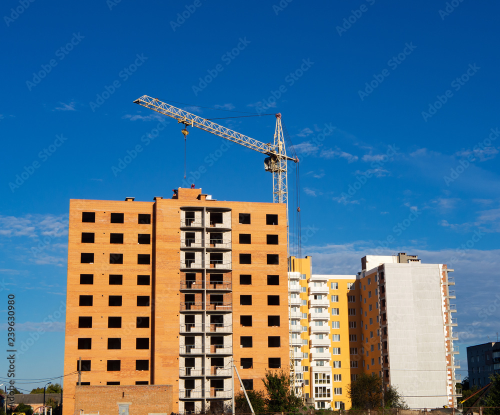 Brick multistory building with holes for windows under construction under blue sky, new condominium on the background