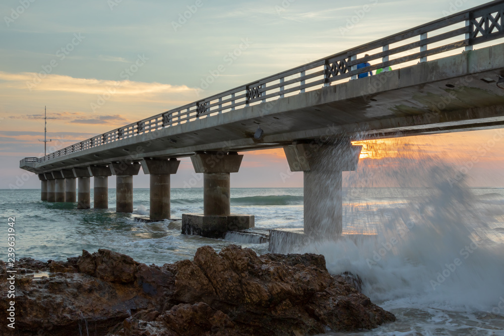 Pier in the sea at sunrise with splashing wave