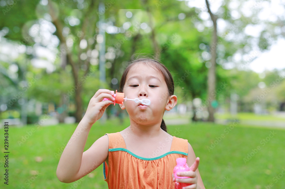 Asian little girl blowing soap bubbles in green park Asian little girl blowing soap bubbles in green park